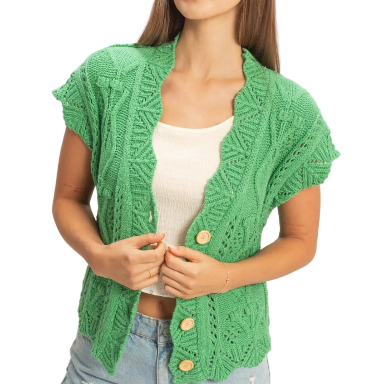 Woman wearing a green knitted cardigan over a white top and denim shorts on a plain background