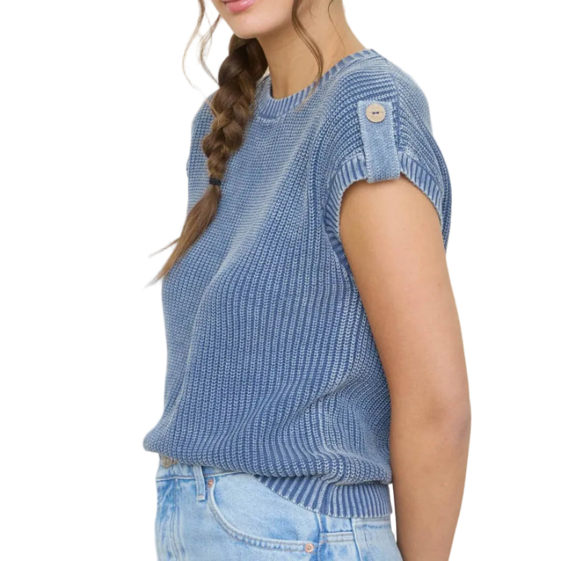 Woman wearing a blue ribbed sweater and light blue jeans standing in front of framed artwork on a white wall.