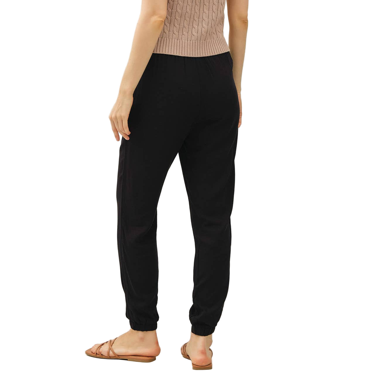 Woman wearing a beige sleeveless top and black pants on a white background