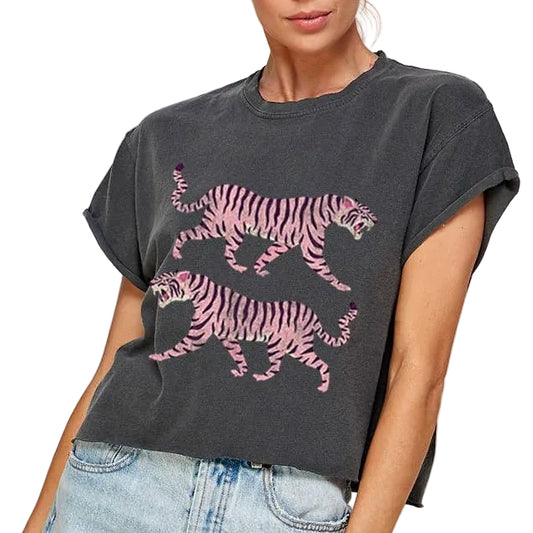 Woman wearing a dark gray t-shirt with pink tiger design and light blue denim shorts on a plain background