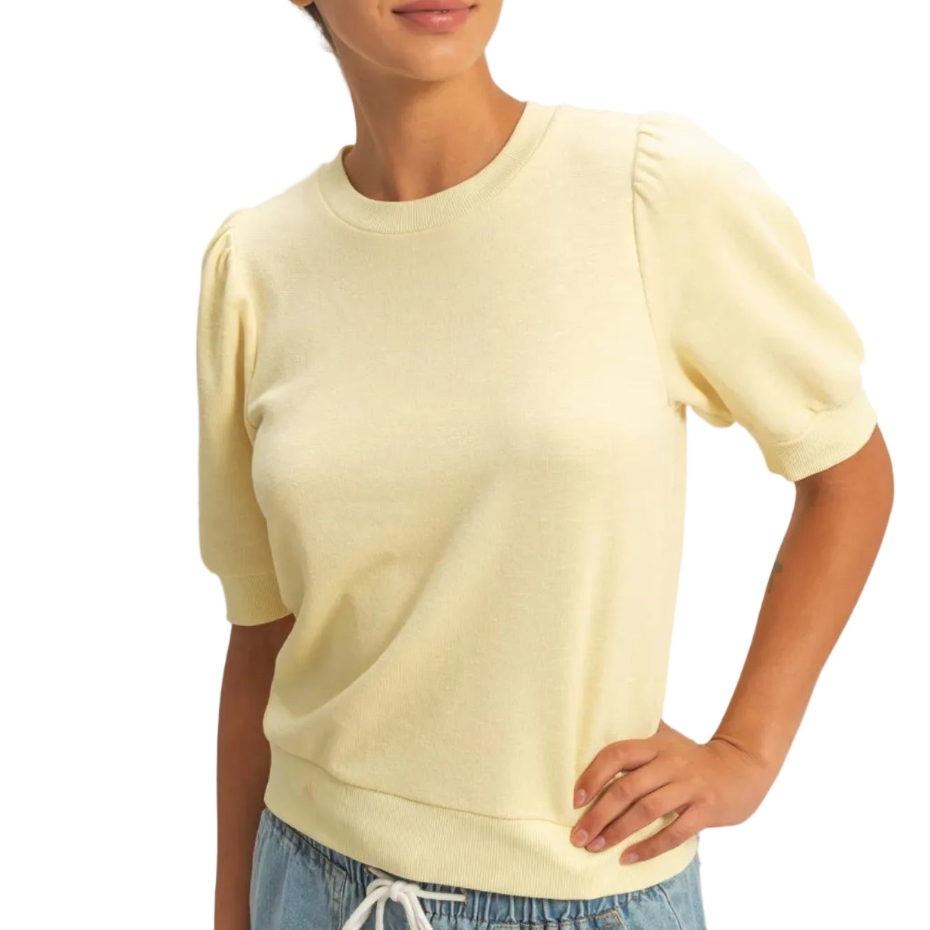 Woman wearing a light yellow top and blue jeans against a plain background