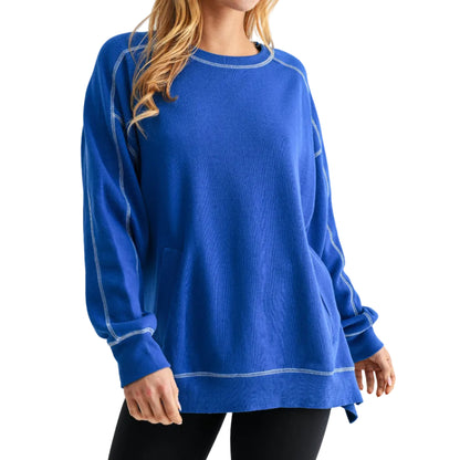 Woman wearing a blue sweatshirt and black cap with a white visor on a light gray background