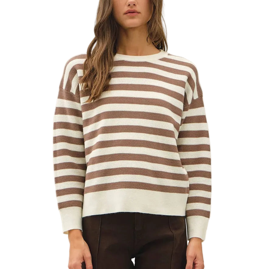 A woman modeling a brown and cream striped knit sweater with dark brown wide-leg trousers and tan lace-up shoes, standing against a plain white studio background.
