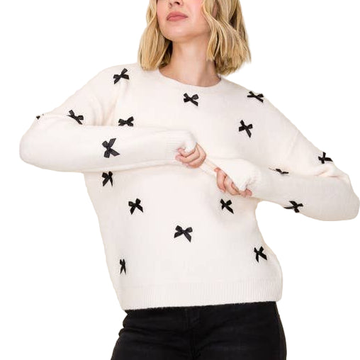 Woman wearing a white sweater with black patterns, black pants, and black boots against a beige background