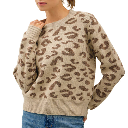 Woman wearing a beige sweater with brown leopard print and blue jeans on a light gray background