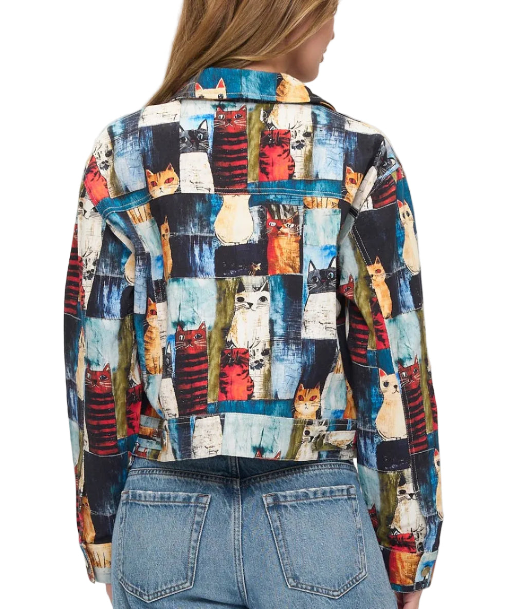 A woman viewed from the back wearing a long-sleeve button-up shirt with a colorful patchwork print of various cat illustrations, paired with light-wash blue jeans against a plain white background.