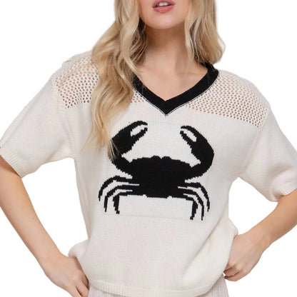 Woman wearing a white sweater with a black crab design on a plain background