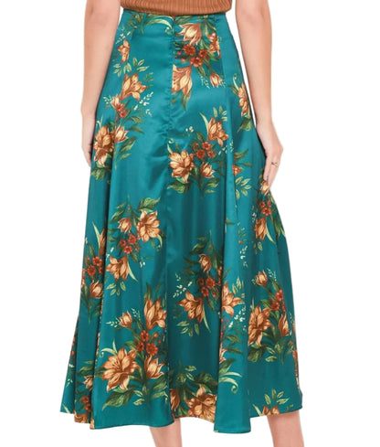 A model is shown from the waist down wearing a teal satin midi skirt with a large orange and green floral print, paired with a brown ribbed top and brown pointed-toe mule heels.