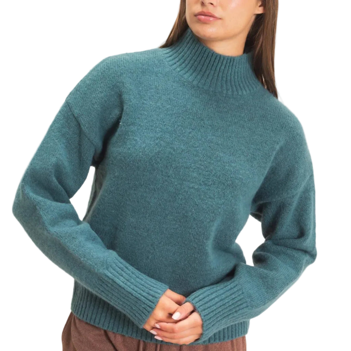 A woman wearing a teal blue-green ribbed mock-neck knit sweater and brown drawstring sweatpants, standing against a plain light beige studio background.