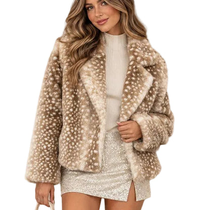 A woman models a beige faux fur jacket with white spots, styled with a white top, a silver sequin mini skirt, and white boots, holding a small cream handbag against a neutral beige background.