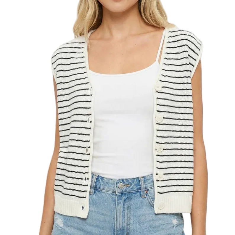 Woman wearing a striped vest over a white top and blue jeans on a light pink background