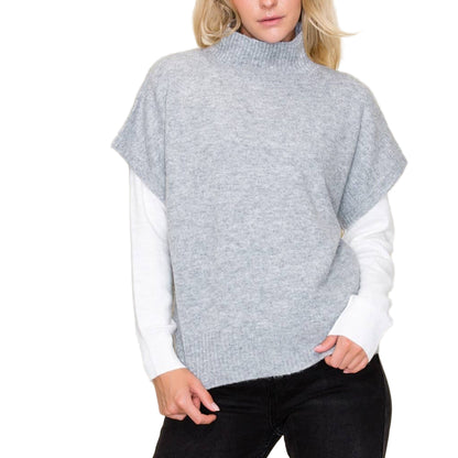 Woman wearing a gray poncho over a white shirt with a beige background