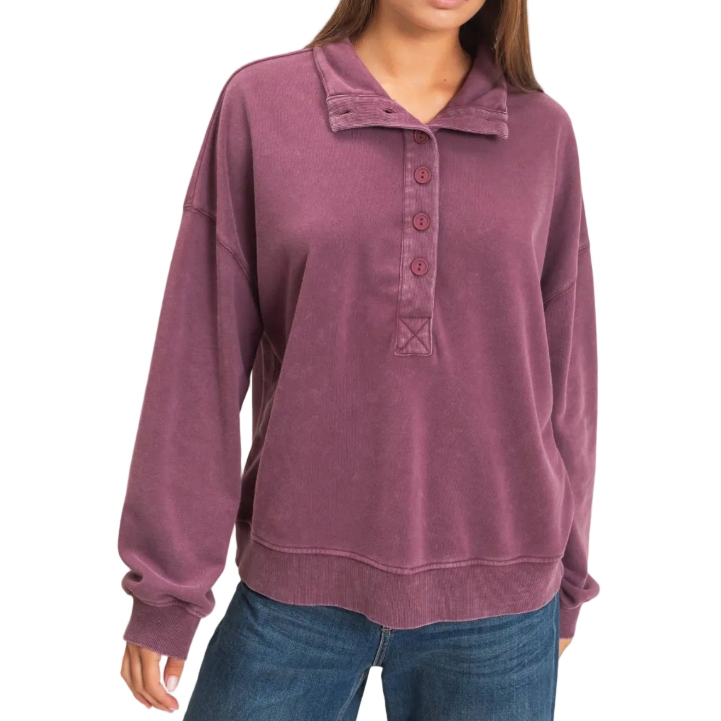 A woman wearing a dusty mauve long-sleeve polo sweatshirt with a button placket and blue jeans, standing against a plain light beige background.
