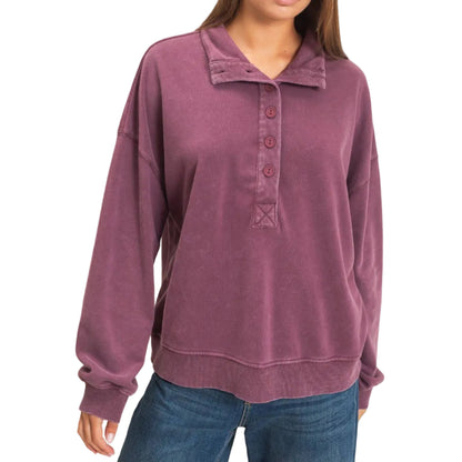 A woman wearing a dusty mauve long-sleeve polo sweatshirt with a button placket and blue jeans, standing against a plain light beige background.