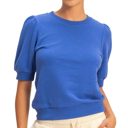 Woman wearing a blue sweater and beige pants against a plain background