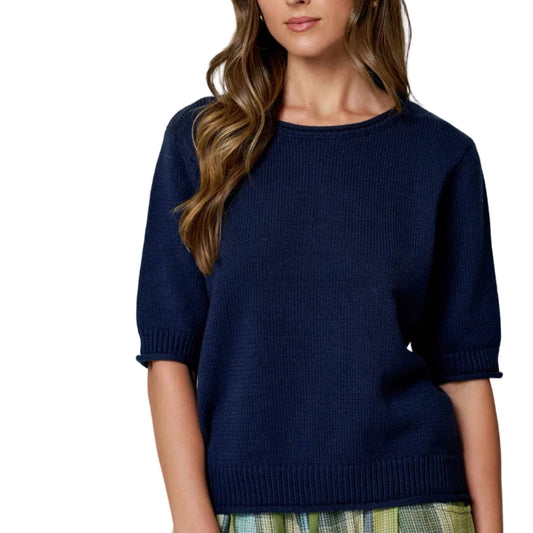 Woman wearing a navy sweater and plaid skirt against a plain background