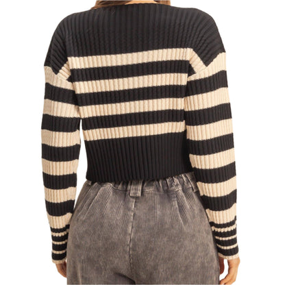 Person wearing a black and beige striped sweater with gray pants on a beige background