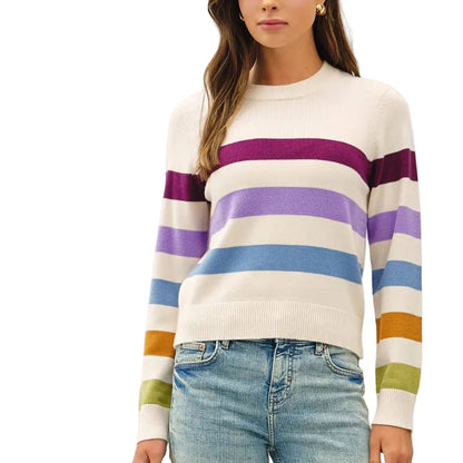 A woman modeling a cream knit sweater with horizontal purple, blue, and orange stripes on the sleeves, paired with light-wash flare jeans and tan shoes, against a plain white studio background.