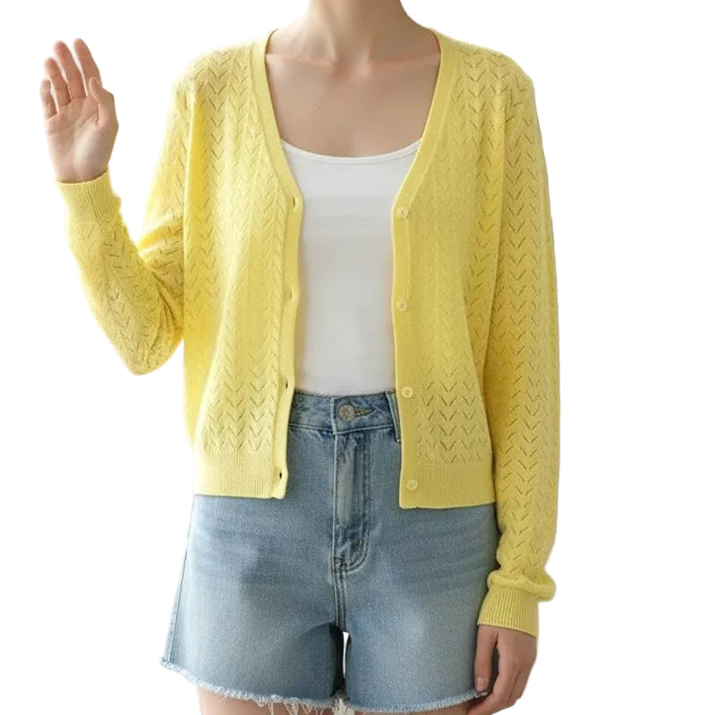 Woman wearing a yellow cardigan over a white top and denim shorts in a bright room with a plant.