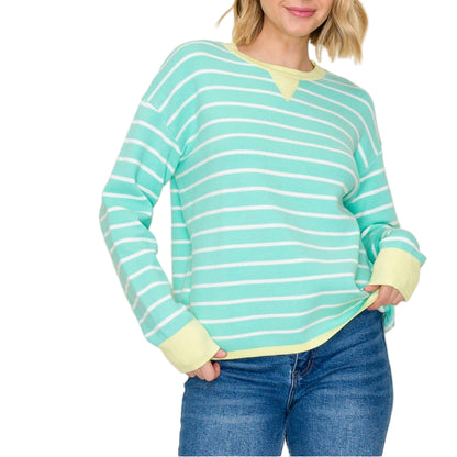 Woman wearing a green and white striped sweater with yellow cuffs and hem against a plain background