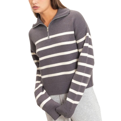 A woman wearing a gray and white horizontally striped half-zip knit sweater with gray sweatpants, photographed against a plain light beige studio background.