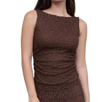 A woman modeling a sleeveless black lace midi dress with a gathered bodice and flared skirt, paired with black ankle boots, standing against a light gray wall and concrete floor.