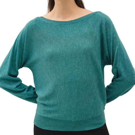 A woman wearing a teal green knit sweater with a wide boat neckline and long sleeves, paired with black pants, against a plain light gray background.