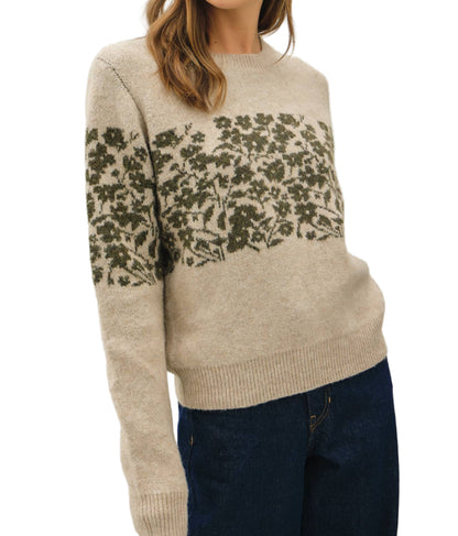 Woman wearing a beige sweater with floral pattern on a plain background