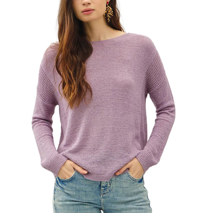 Woman wearing a purple sweater and light blue jeans against a plain background
