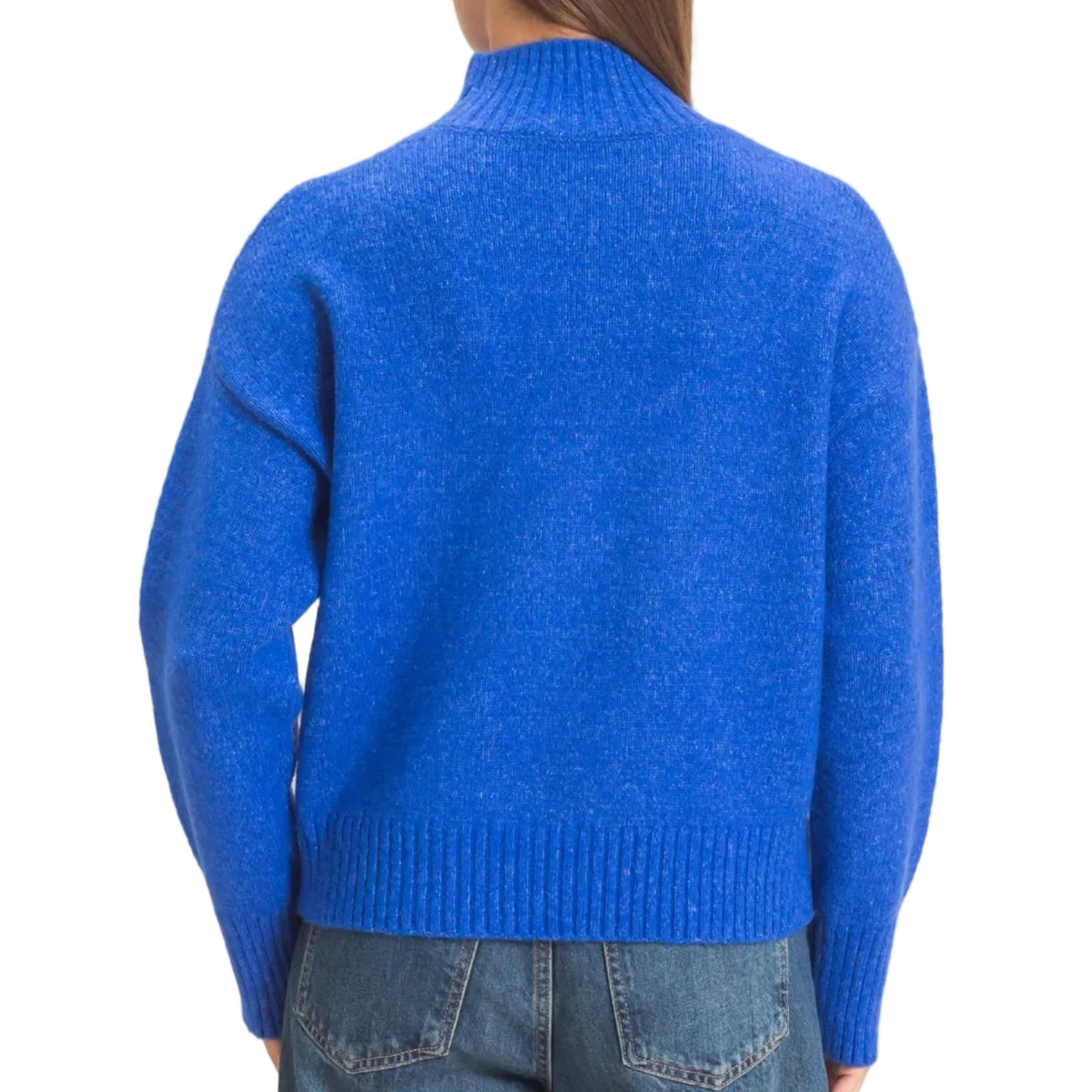 A woman viewed from the back wearing a bright royal blue knit mock-neck sweater and blue jeans against a plain light beige studio background.
