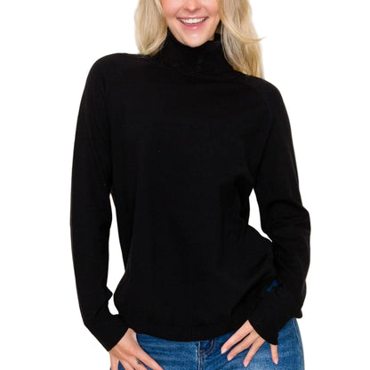Woman wearing a black turtleneck sweater and blue jeans against a plain background