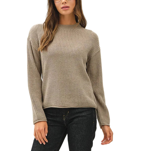 A woman modeling a beige ribbed knit sweater, dark wash jeans, and navy sneakers against a plain white studio background.