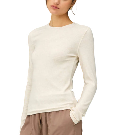 Woman wearing a white long-sleeve top and beige pants against a black background