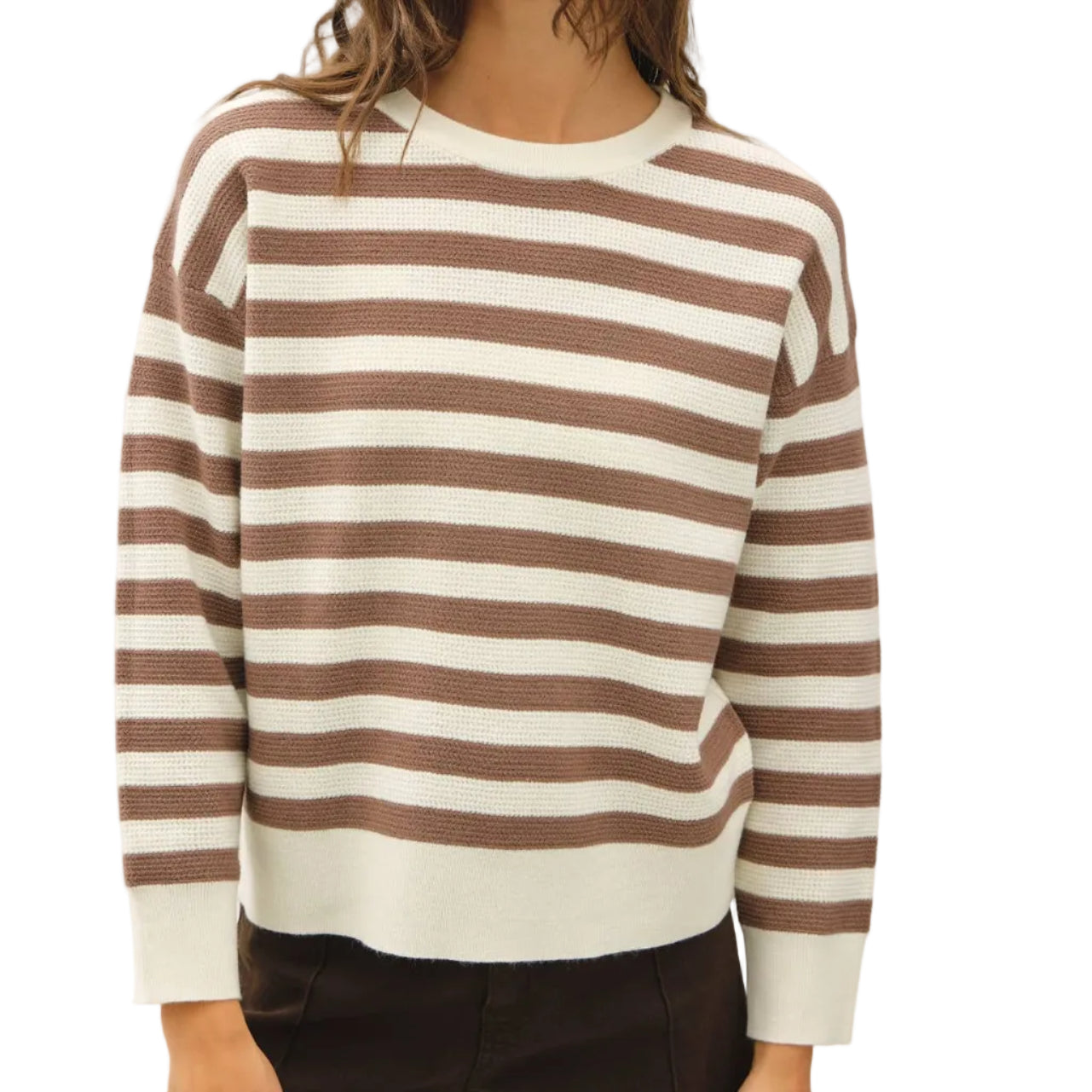 A woman wearing a brown and off-white horizontally striped long-sleeve knit sweater, paired with dark brown pants, against a plain light gray studio background.