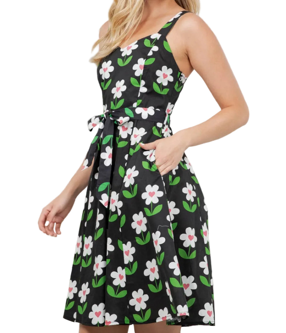 Woman wearing a black floral dress standing indoors with plants in the background