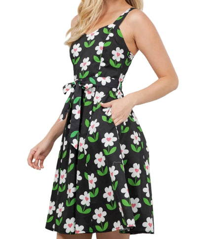 Woman wearing a black floral dress standing indoors with plants in the background