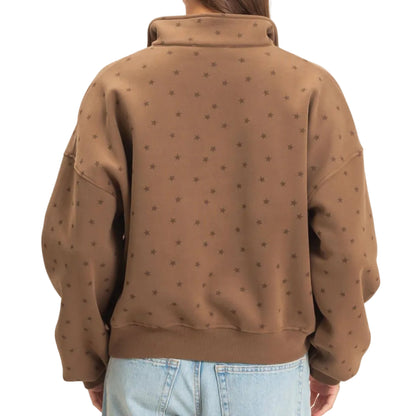 A woman viewed from behind wearing a brown cropped sweatshirt with a subtle repeating star pattern and light-wash blue jeans, set against a plain off-white background.