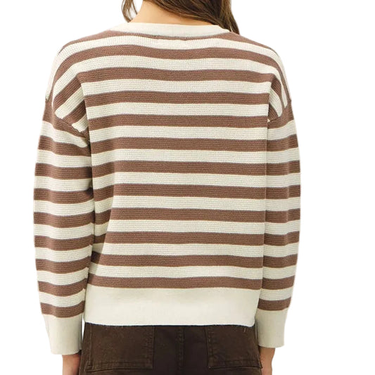 A woman viewed from behind wearing a brown and cream striped long-sleeve sweater and dark brown wide-leg trousers, standing against a plain off-white wall.