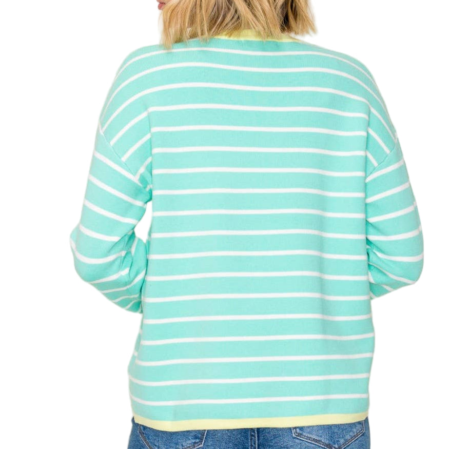 Person wearing a turquoise and white striped sweater with blue jeans on a plain background