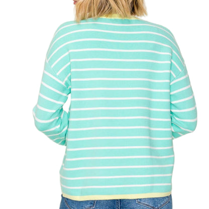Person wearing a turquoise and white striped sweater with blue jeans on a plain background