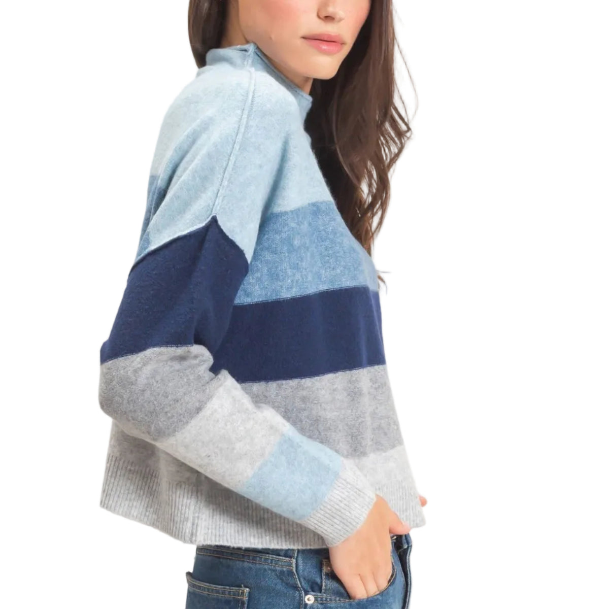 A woman modeling a color-blocked knit sweater with horizontal stripes in light blue, navy, and heather gray, paired with blue jeans against a plain off-white studio background.