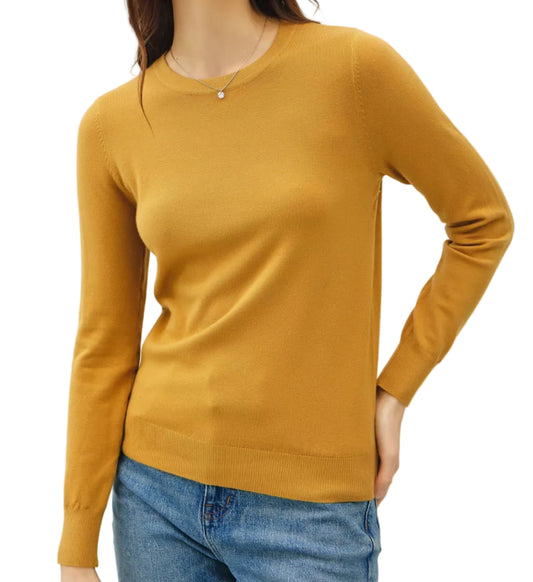 Woman wearing a mustard yellow sweater and blue jeans against a plain background