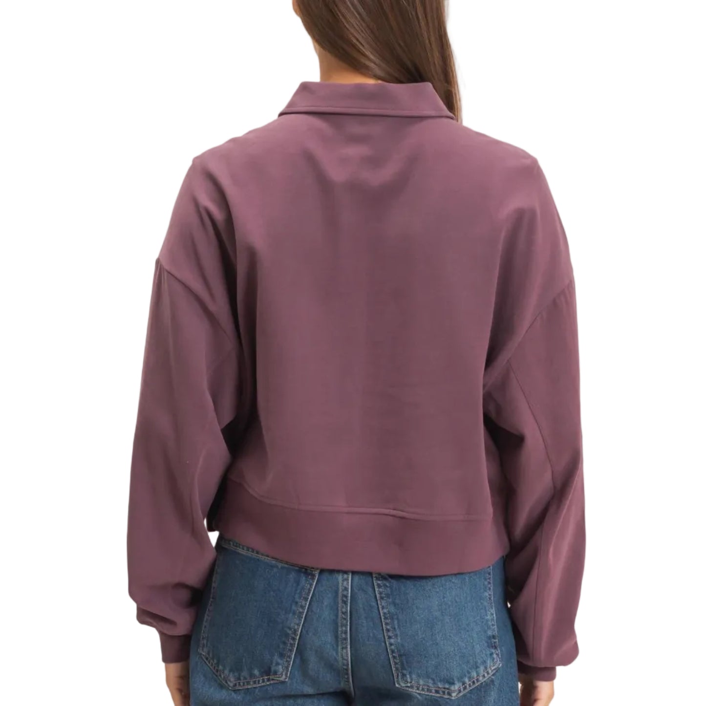 A woman viewed from the back wearing a cropped, long-sleeve collared sweatshirt in a muted mauve-purple color, paired with blue jeans, against a plain light beige background.
