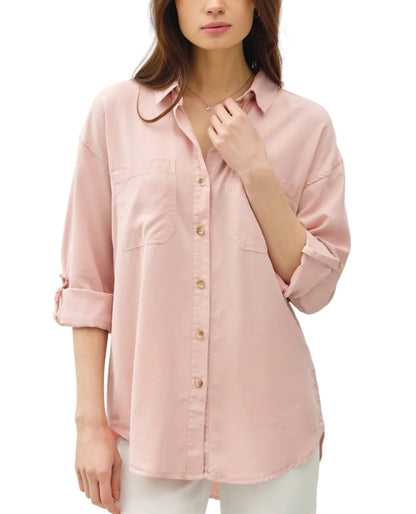 Woman wearing a pink button-up shirt with rolled-up sleeves on a plain background