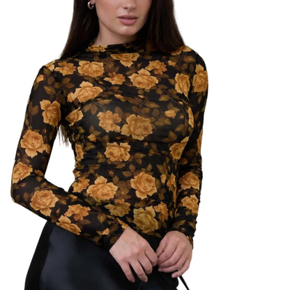 Woman wearing a black floral top and black skirt holding a black handbag against a textured beige wall.