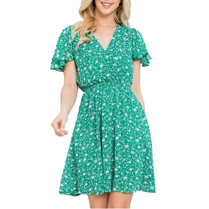 Woman wearing a green floral dress in a bright room with white curtains and a white chair.