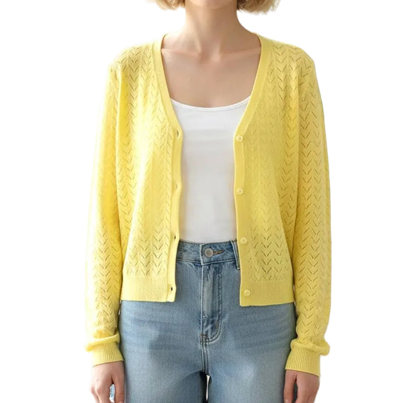 Woman wearing a yellow cardigan, white top, and denim shorts in a bright room with a plant.