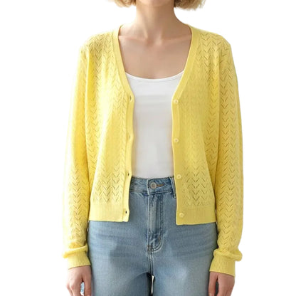 Woman wearing a yellow cardigan, white top, and denim shorts in a bright room with a plant.