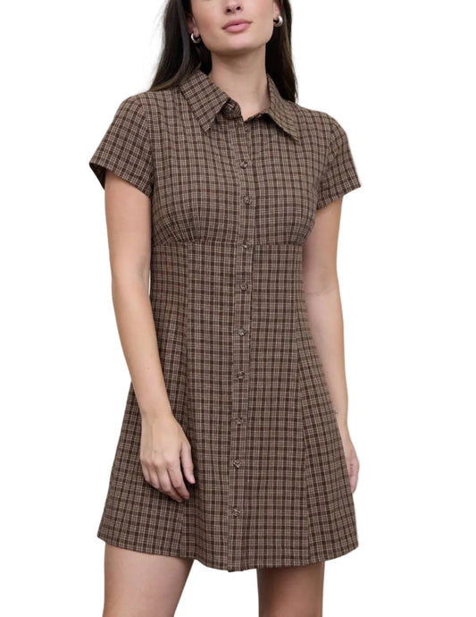 A woman modeling a short-sleeve button-front shirt dress with a brown and black checkered pattern, set against a plain light gray studio background.