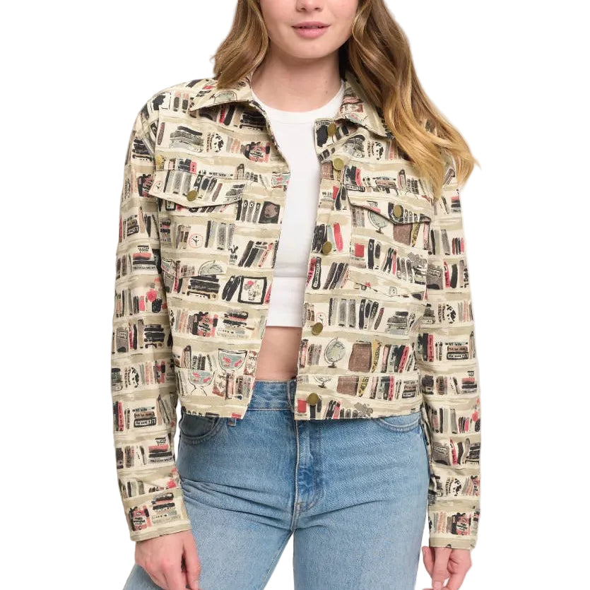 A woman modeling a cropped jacket with an all-over book spine print, styled with a white crop top and blue jeans in a minimalist indoor setting.